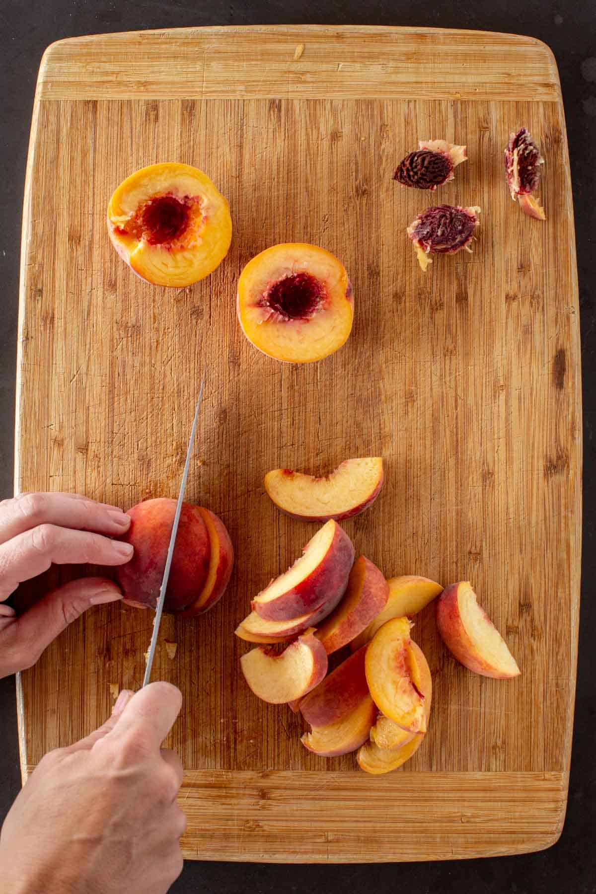A hand slicing fresh peaches on a wooden cutting board.