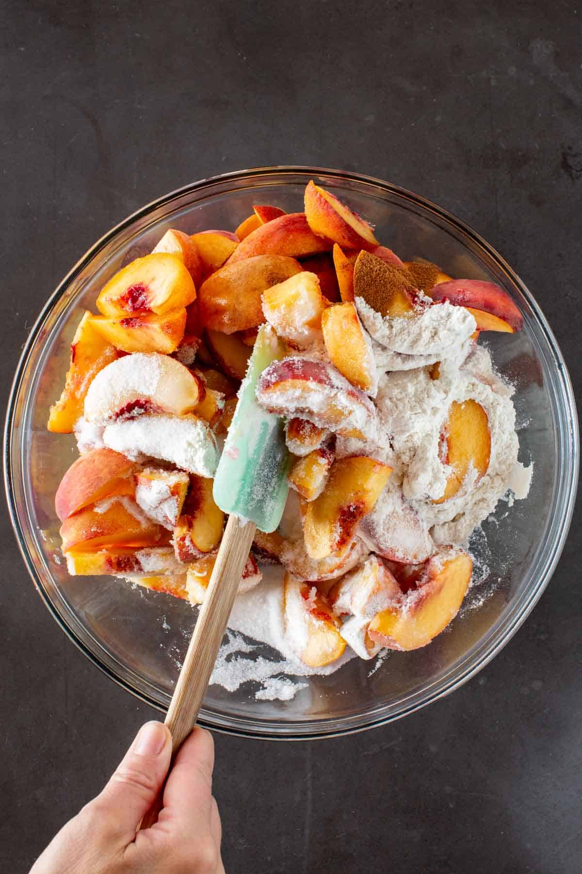 Mixing sliced peaches with sugar and flour in a bowl with a spatula.