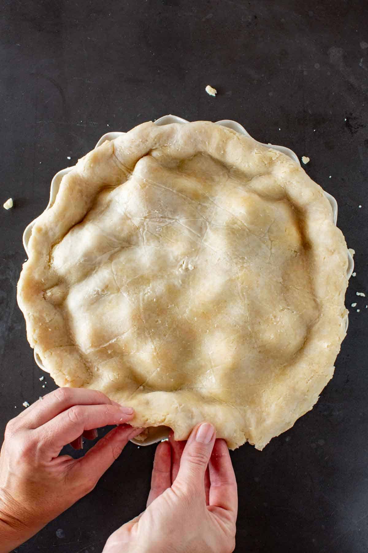 Hands crimping the edges of a pie.