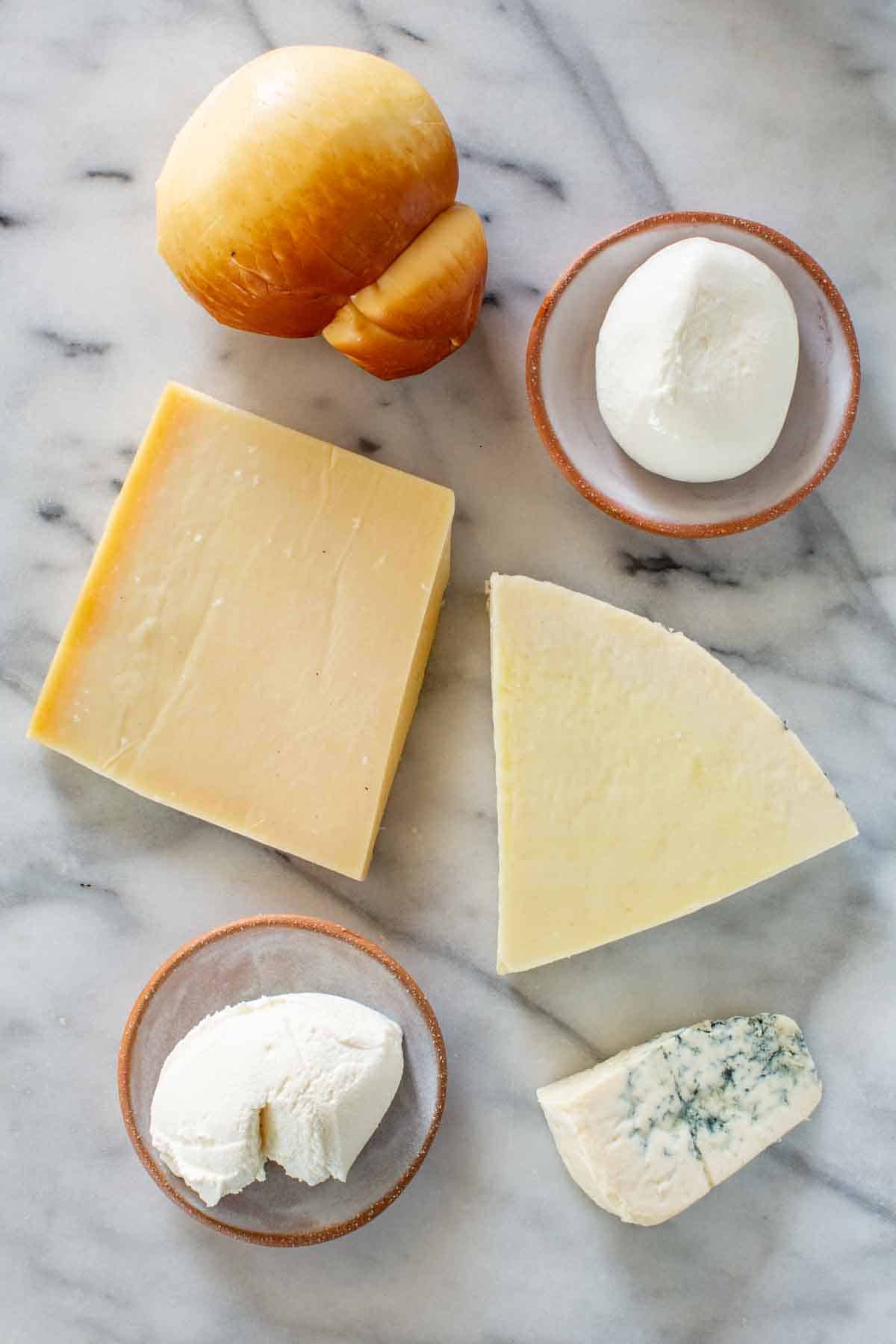 An assortment of hard and soft Italian cheeses on a marble board.