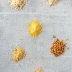 Assorted piles of dry rice and grains on a gray board.