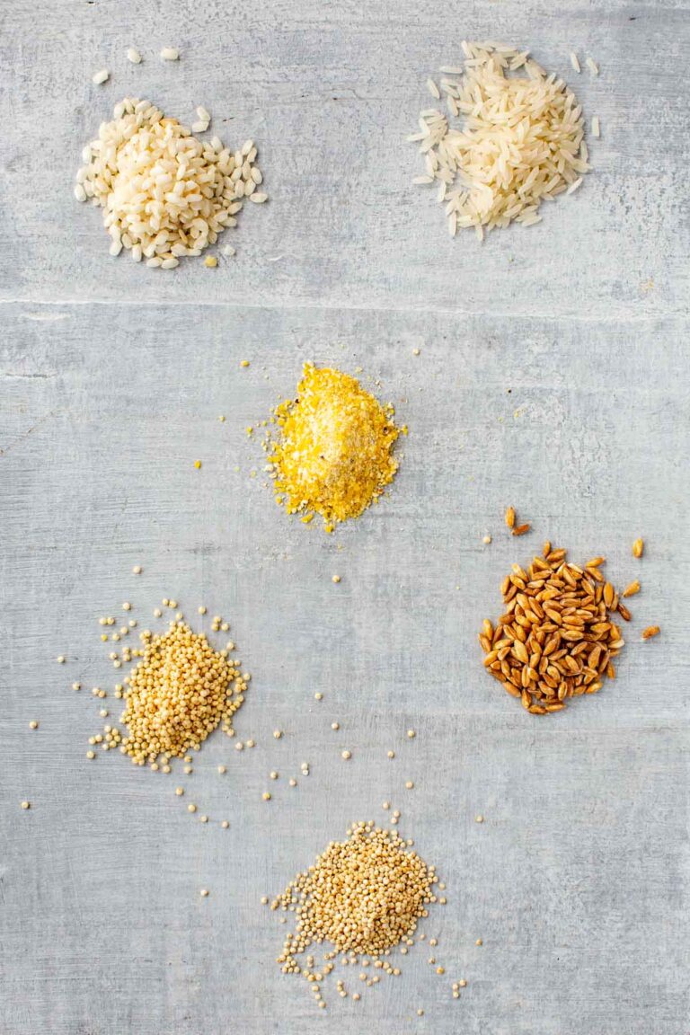 Assorted piles of dry rice and grains on a gray board.