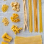 Assorted long and short shapes of pasta arranged on a board.