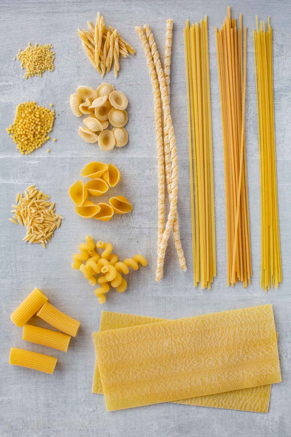 Assorted long and short shapes of pasta arranged on a board.