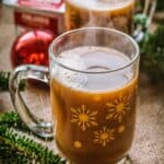 A clear mug with a brown beverage inside and christmas decorations in the background.