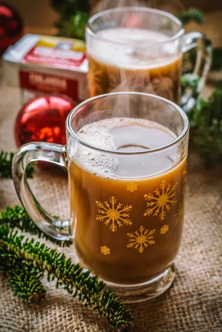 A clear mug with a brown beverage inside and christmas decorations in the background.