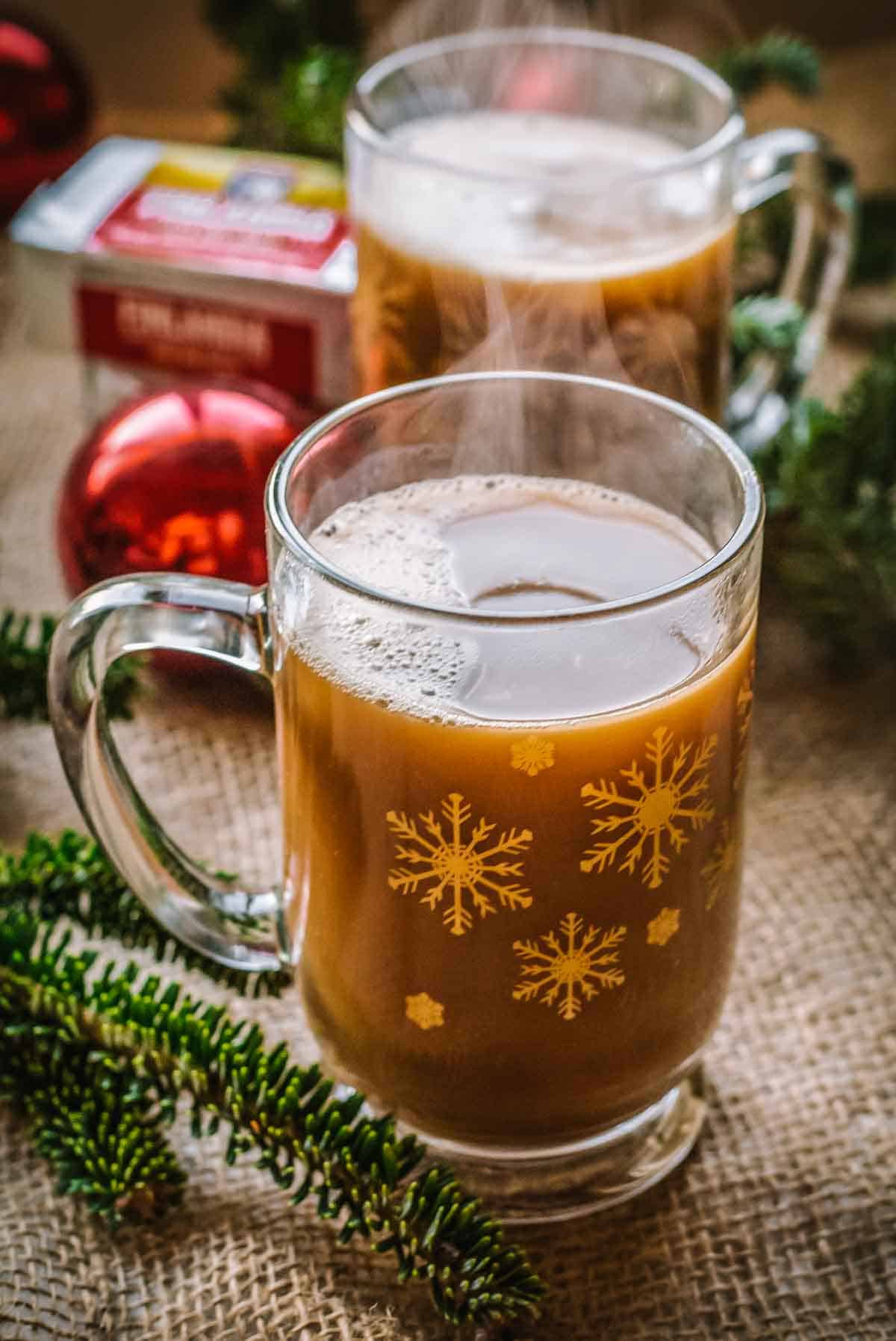 A clear mug with a brown beverage inside and christmas decorations in the background.