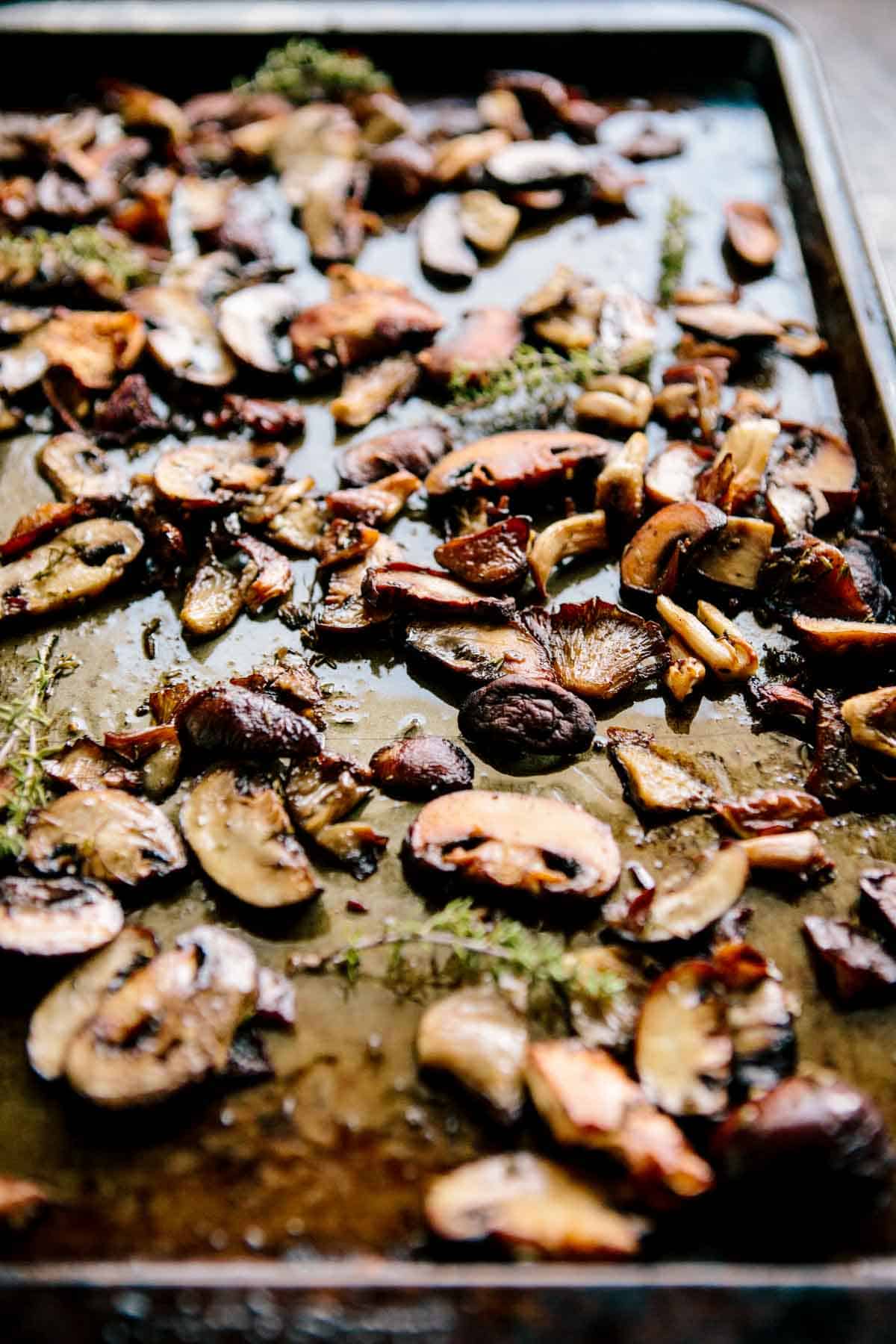 A baking sheet filled with sliced mushrooms and fresh herbs that have been roasted.
