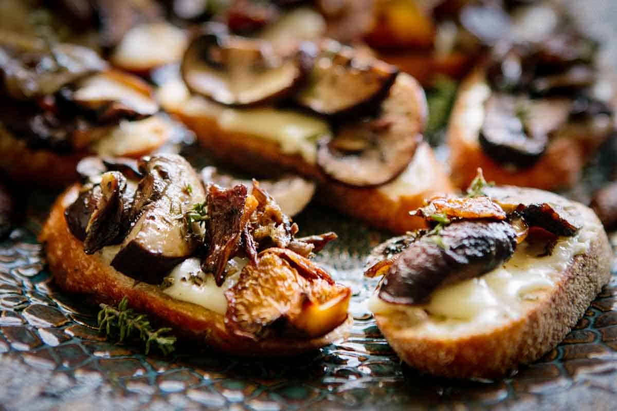 Pieces of crostini on a serving platter topped with goat cheese and roasted mushrooms.