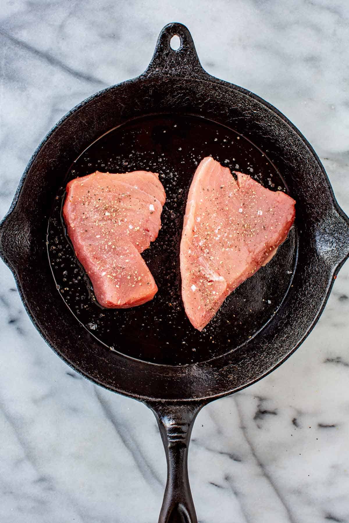 Two tuna steaks searing in a cast iron pan.