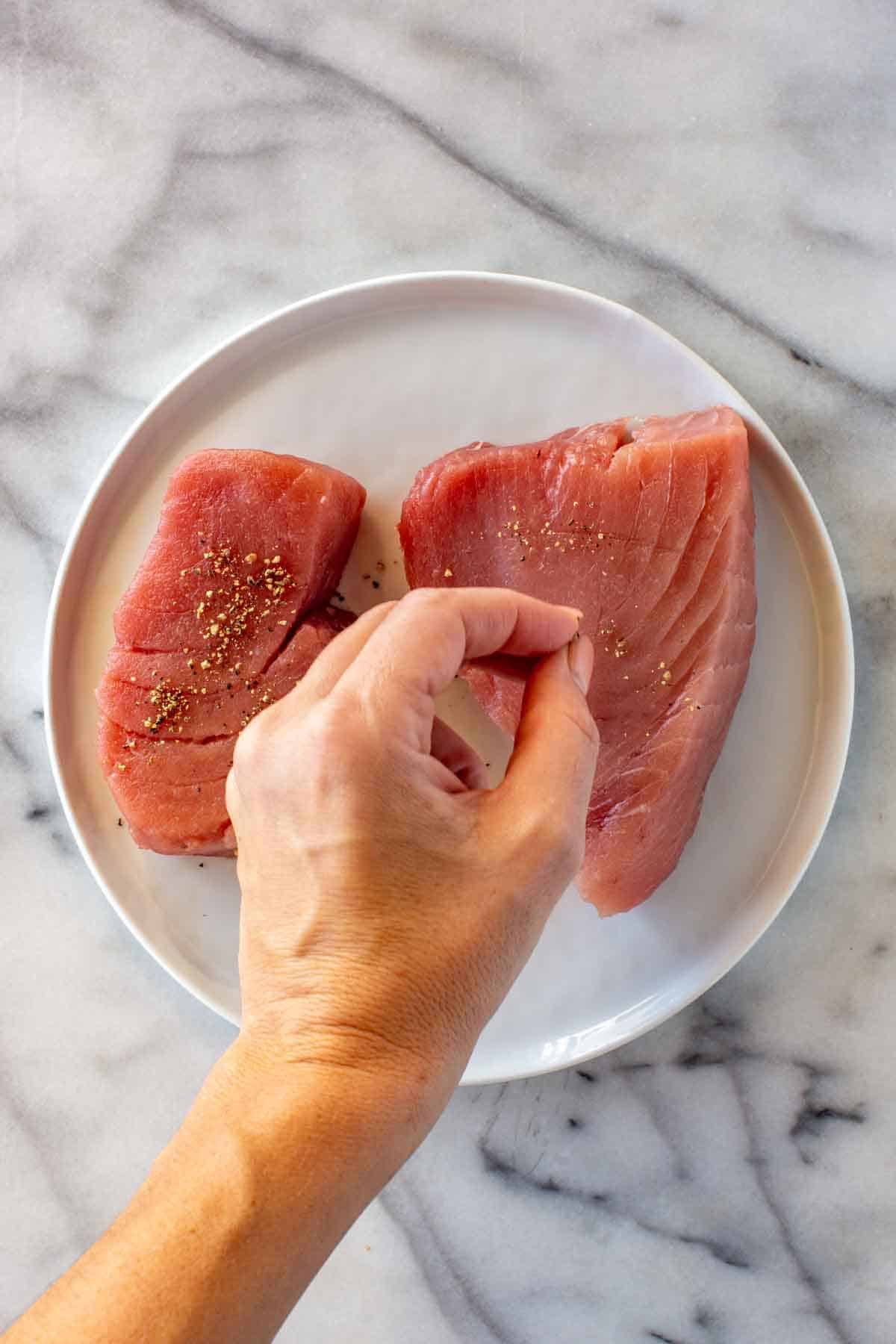 Seasoning tuna steaks with salt and pepper.