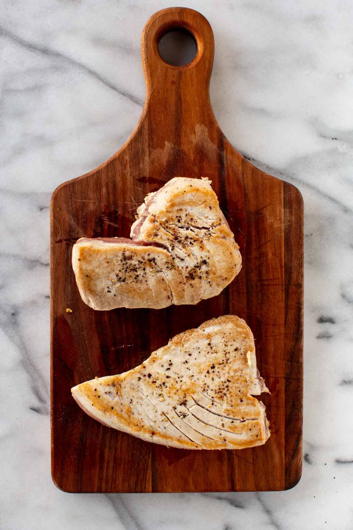 Two seared tuna steaks resting on a wood cutting board.