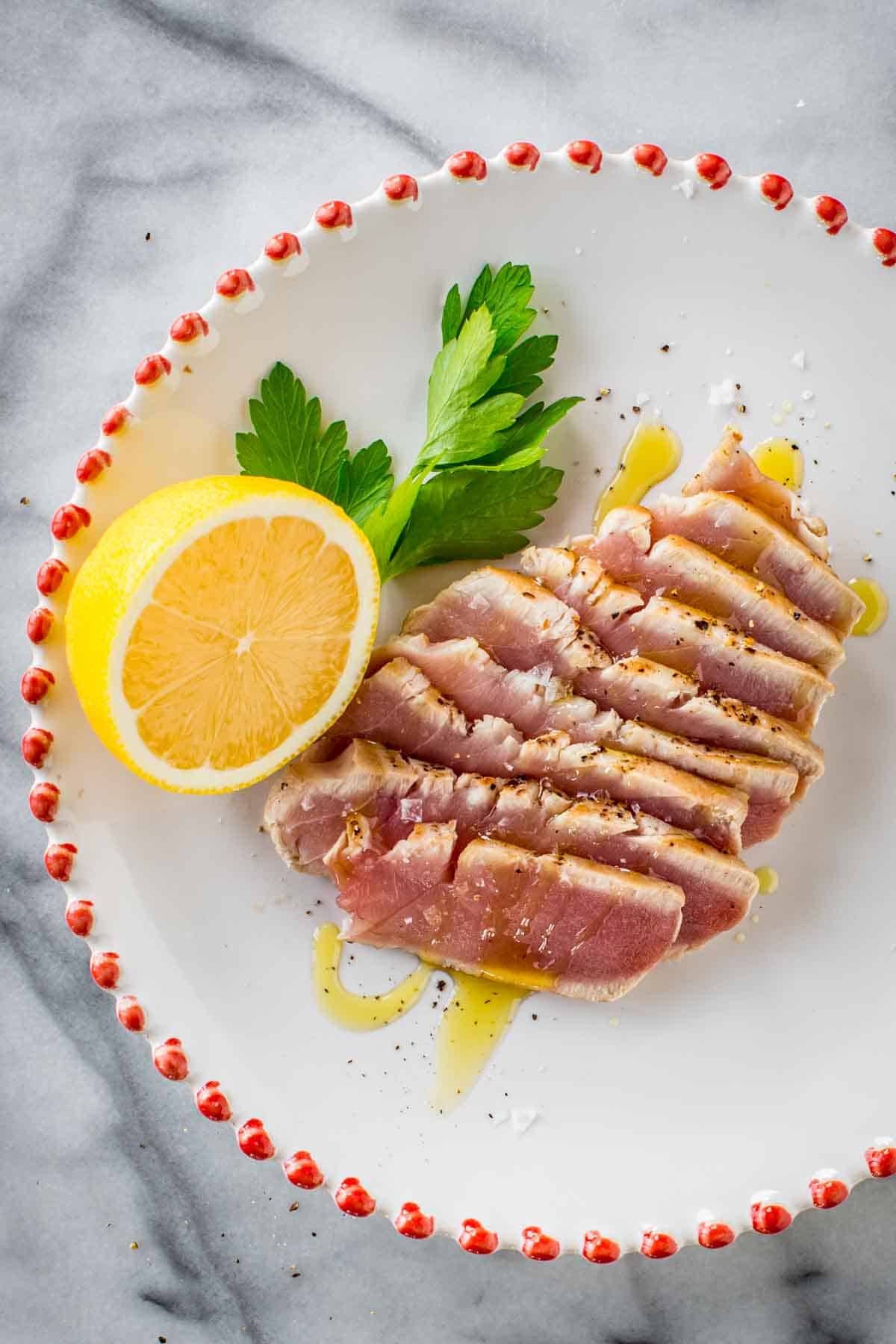 Sliced seared tuna on a plate with a lemon, parsely and olive oil drizzle,