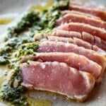 Rare seared tuna sliced on a plate with an herb sauce.