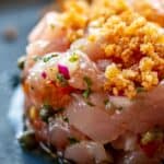 Close up of fresh raw ahi tuna tartare with capers, tomatoes, red onion and breadcrumbs on top.
