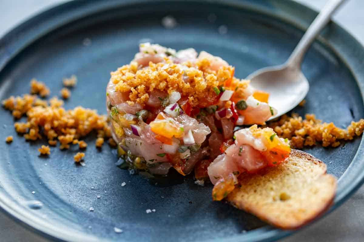 A spoon picking up pieces of tuna tartare on to a piece of bread.