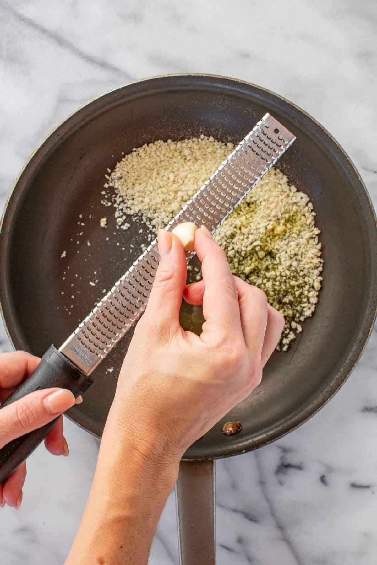 Grating a clove of garlic into a pan of breadcrumbs.