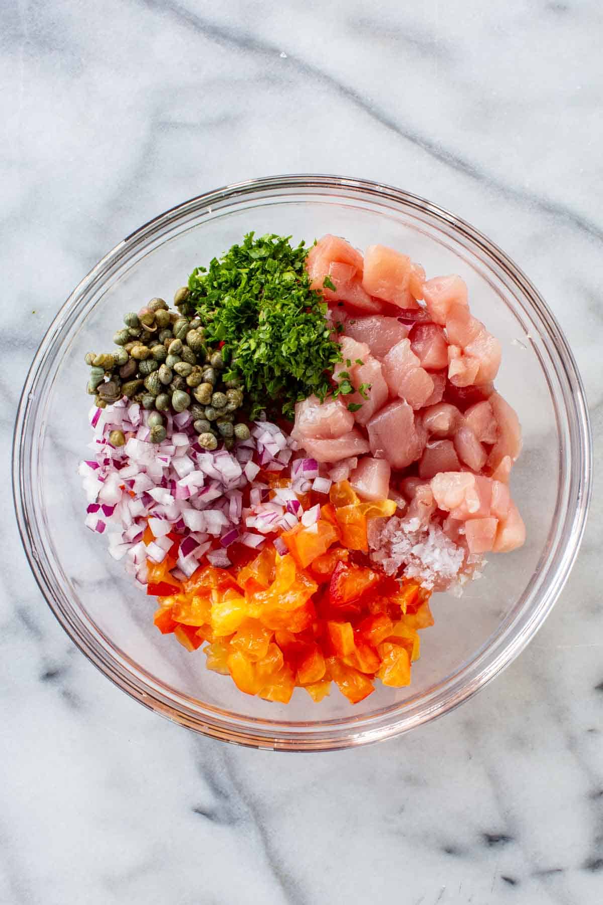 A bowl with raw tuna, onion, tomatoes, capers and parsley.