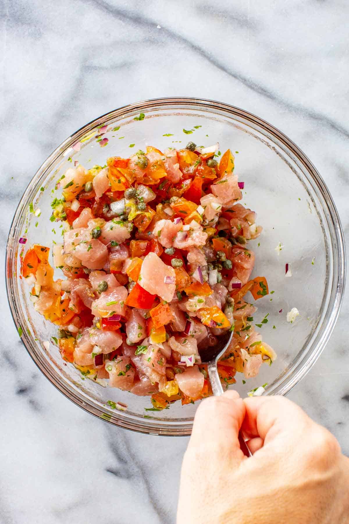 Mixing together raw tuna with tomatoes, capers, red onion and lemon.