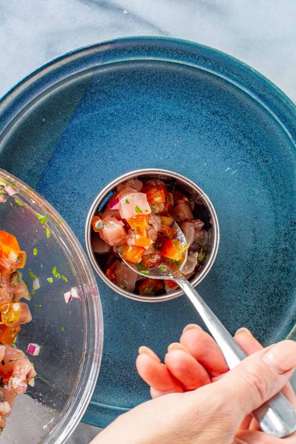 Spooning pieces of tuna into a ring mold.