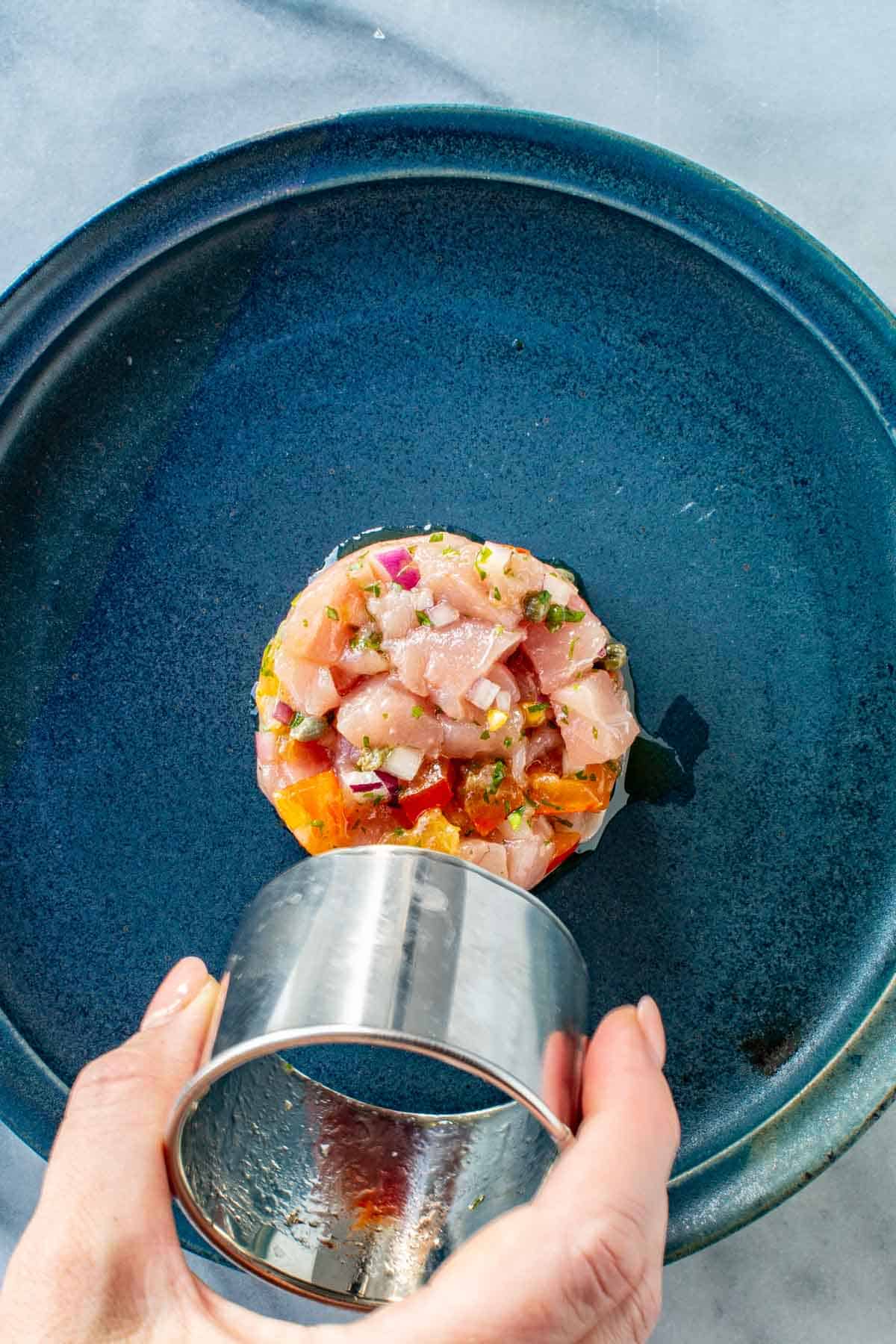 Removing the ring mold from a plate of tuna tartare.
