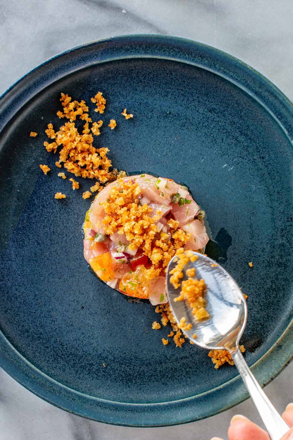 Spooning breadcrumbs over a mound of tuna tartare.