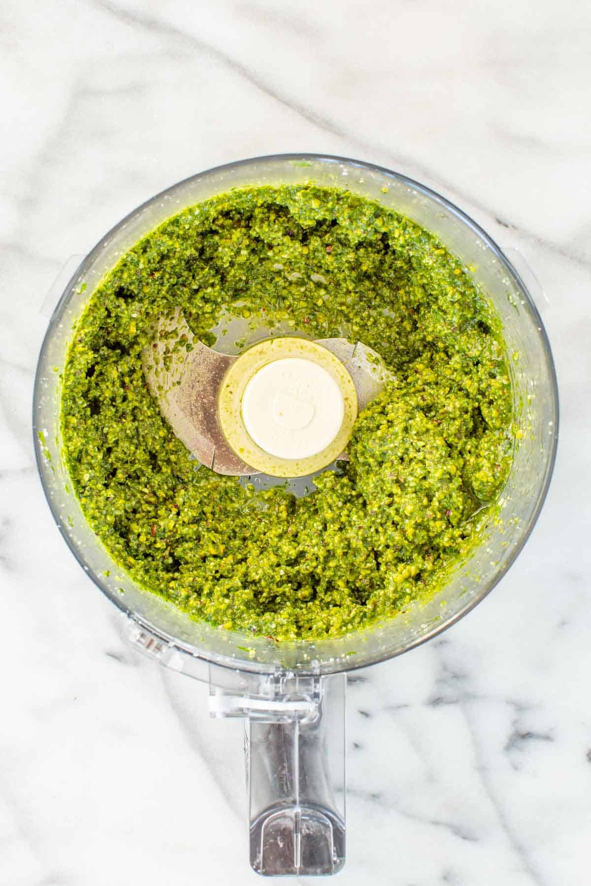 A food processor with blended pesto inside.