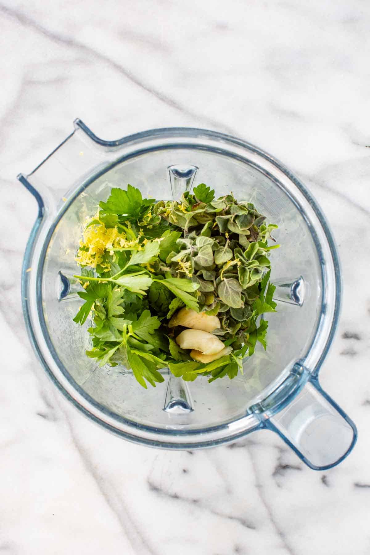 A blender with garlic, herbs and lemon zest.