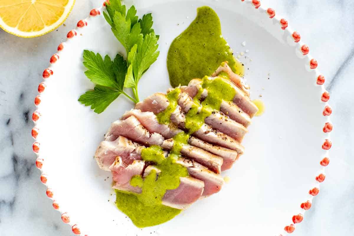 A piece of seared tuna with green sauce and a sprig of parsley.