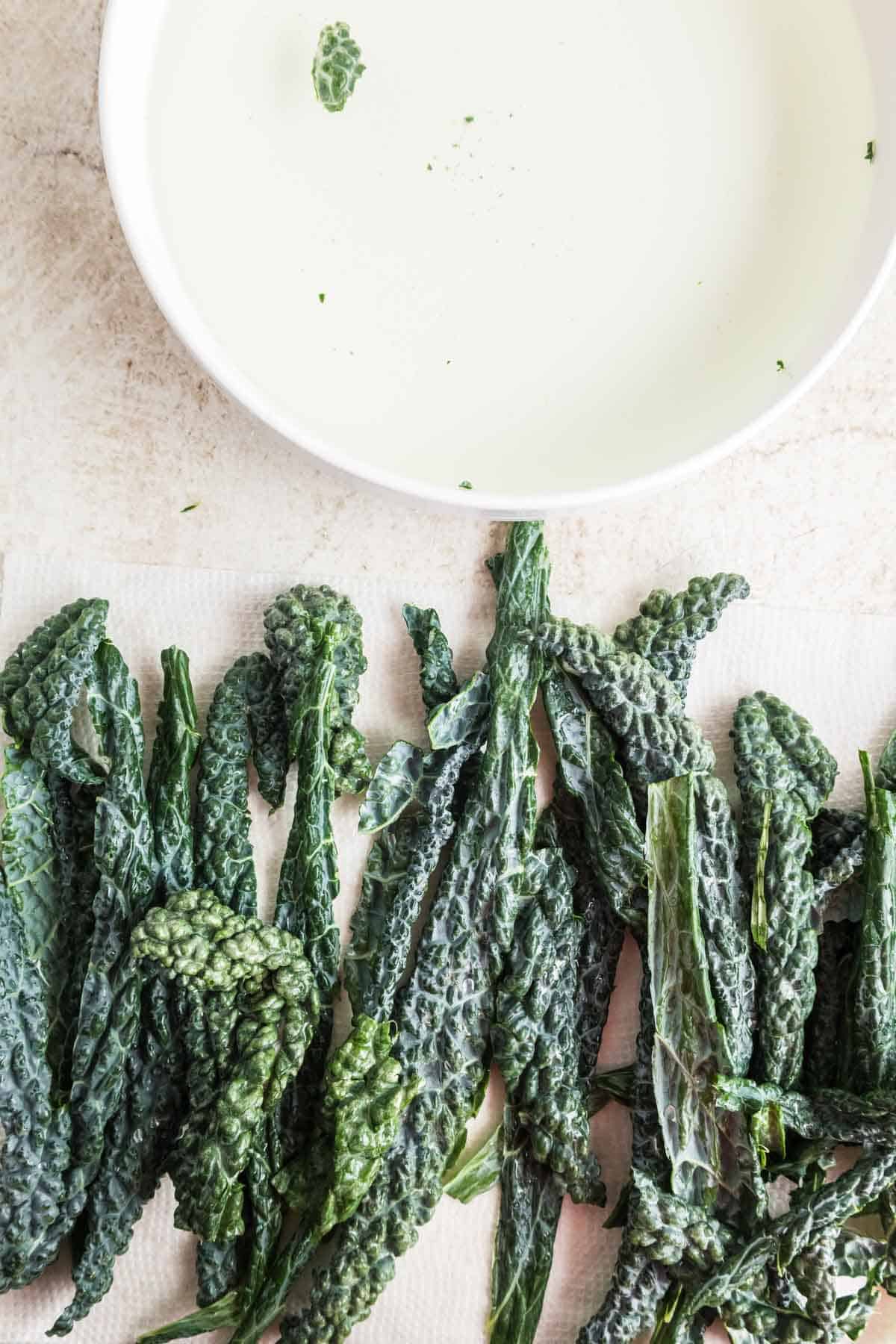 A bowl of water with freshly washed kale leaves next to it.