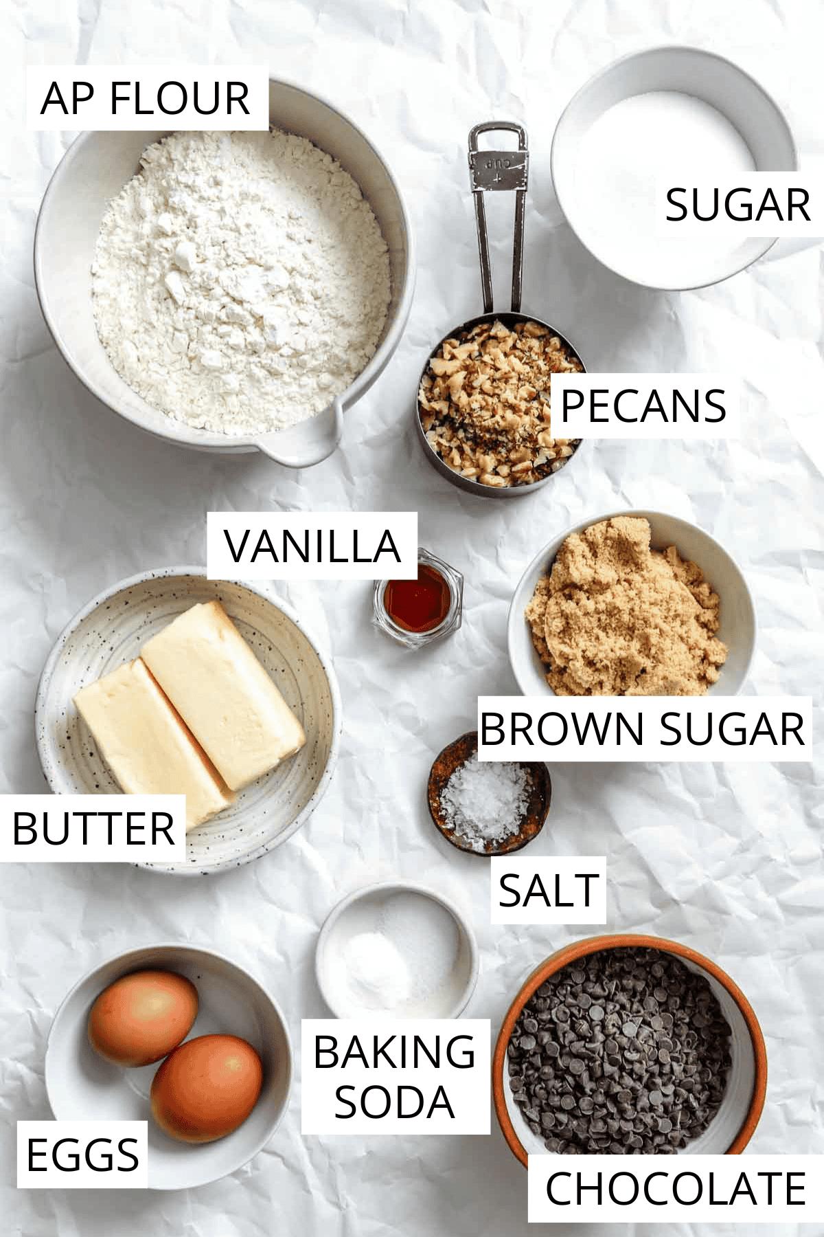 Overhead view of ingredients for chocolate chip cookies including flour, butter, sugar, eggs, vanilla, and chocolate chips.