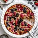 Overhead view of a slice of berry clafoutis on a serving utensil, showing the creamy texture and embedded berries.