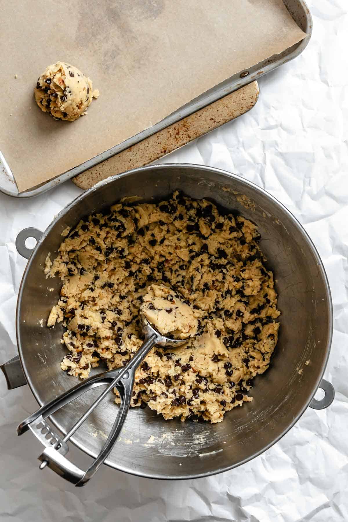 Raw cookie dough with chocolate chips being scooped onto a parchment-lined baking sheet.