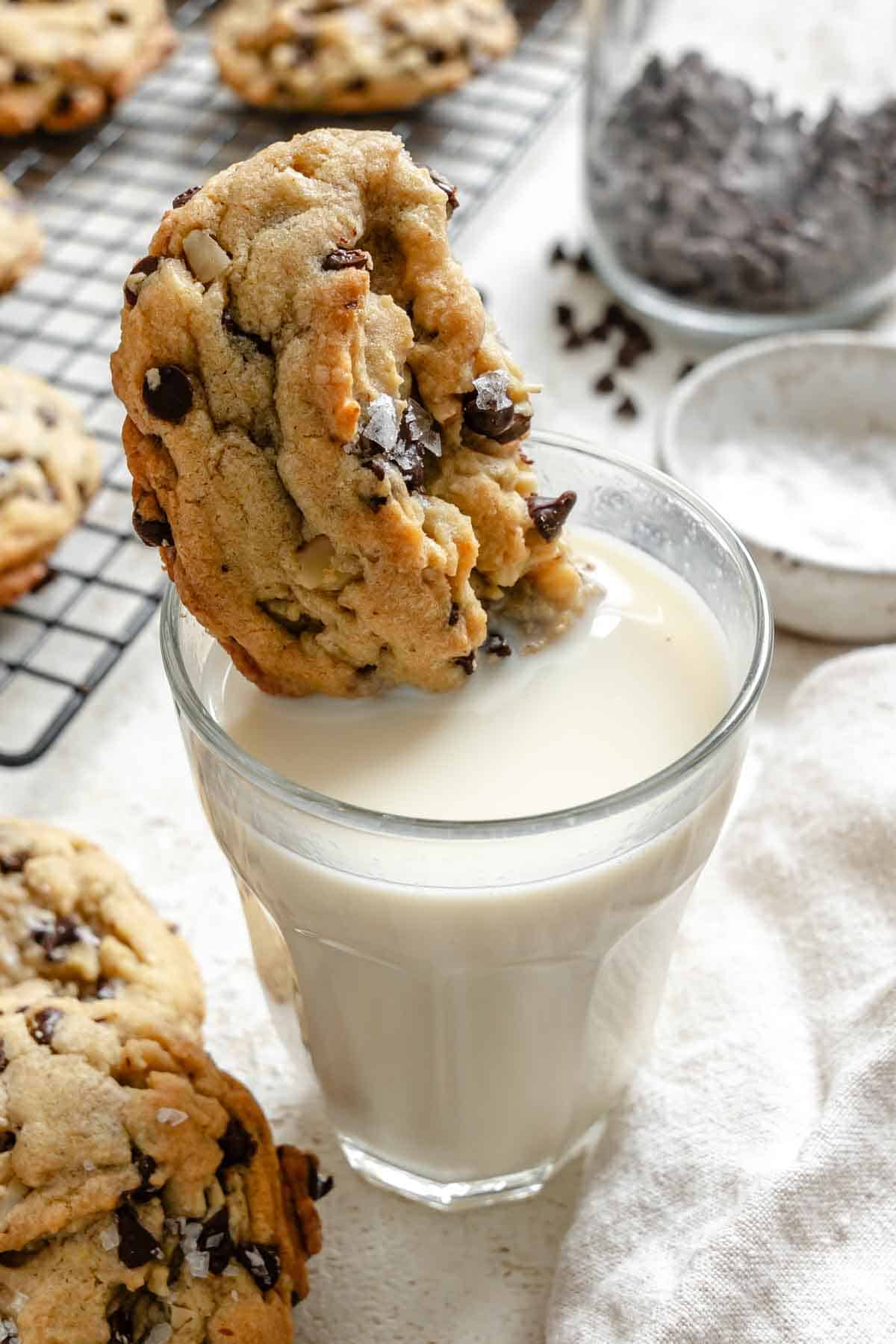 Chocolate chip cookie being dipped into a glass of milk.