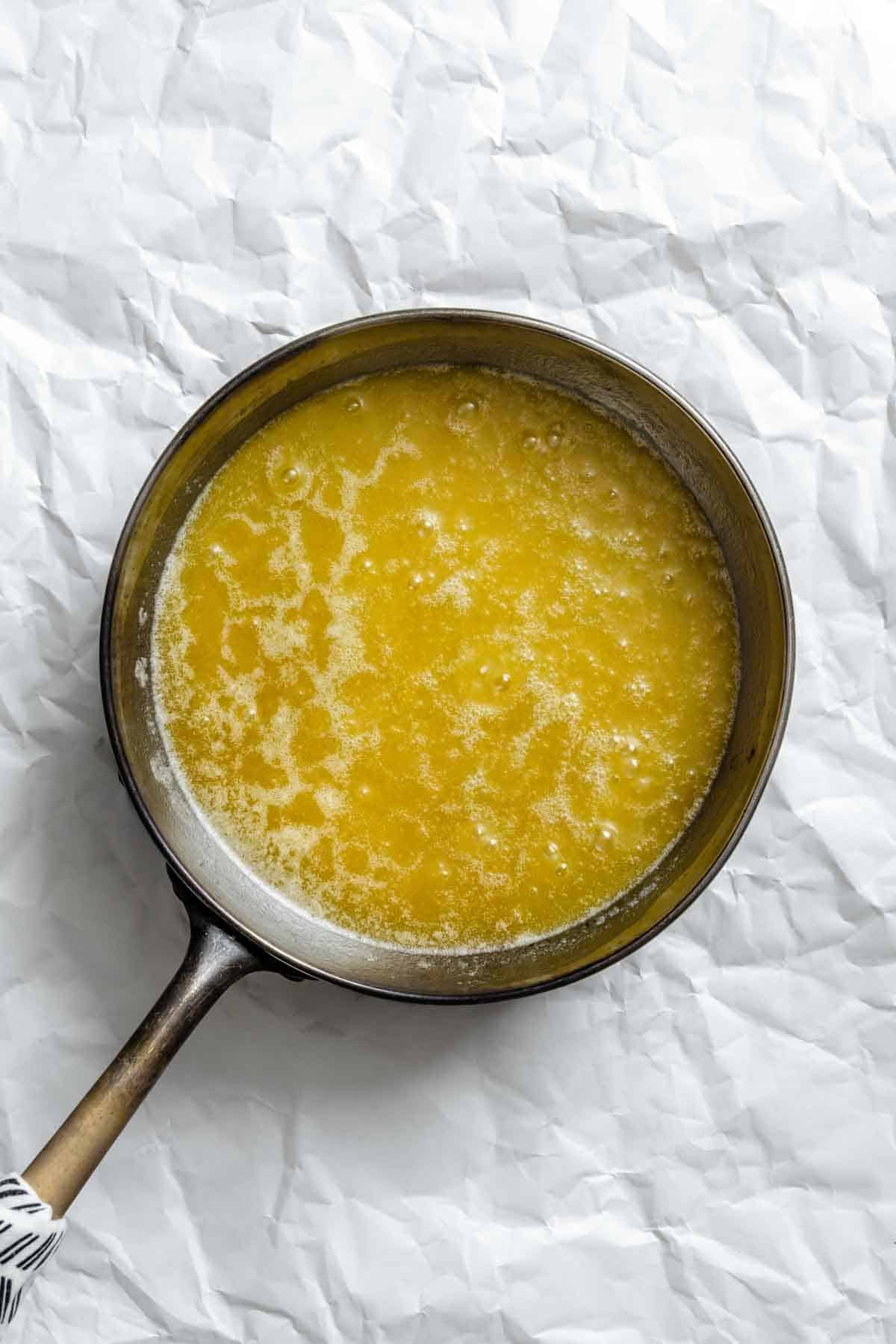 Brown butter melting in a saucepan, showing the golden color and foam on the surface.