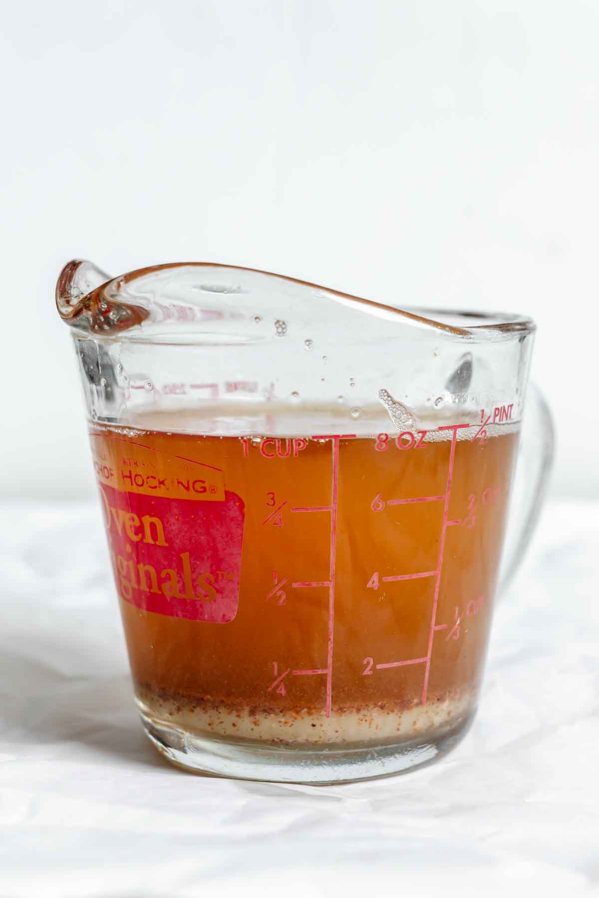 Measuring cup filled with amber-colored brown butter and some sediment at the bottom.