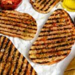 More grilled bread slices on parchment paper with tomatoes, olive oil, and a jar of olive oil in the corner.