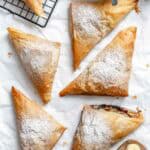 Baked phyllo triangles with powdered sugar, one broken open showing Nutella filling, with banana slices.