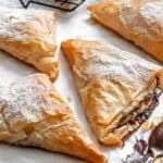 Stacked broken phyllo triangles revealing Nutella filling, dusted with sugar and surrounded by bananas.