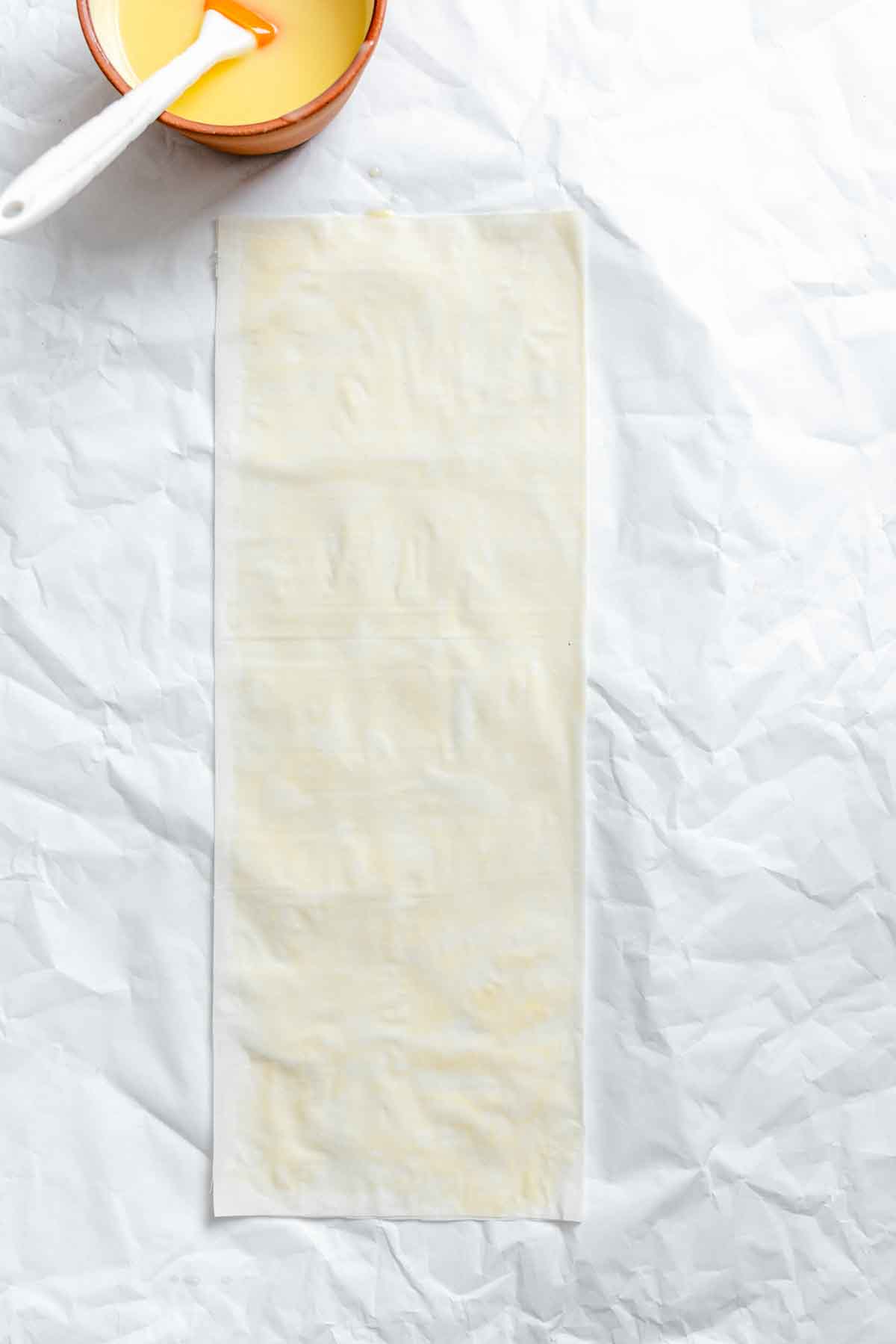 Phyllo sheet on parchment with a bowl of butter and pastry brush at the top.