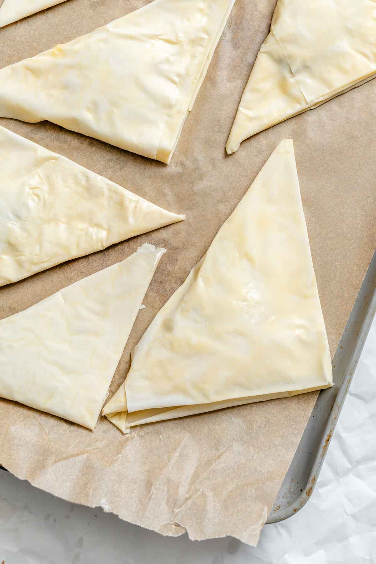 Several unbaked phyllo triangles arranged on parchment on a baking sheet.