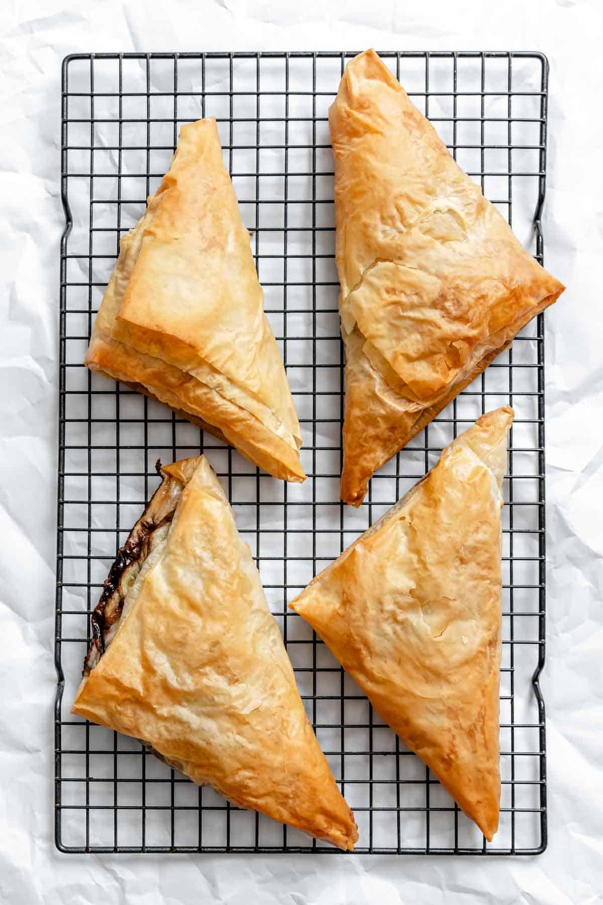 Golden-brown baked phyllo triangles with powdered sugar on a cooling rack.