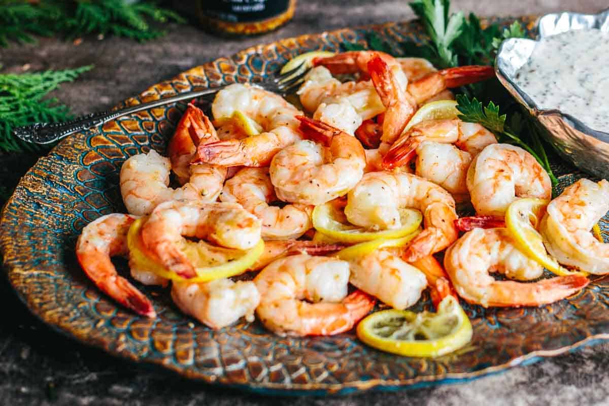 A platter of shrimp cocktail with lemon wheels and a mustard dipping sauce.