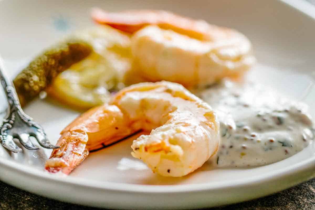 Two pieces of shrimp on a white plate with mustard aioli.