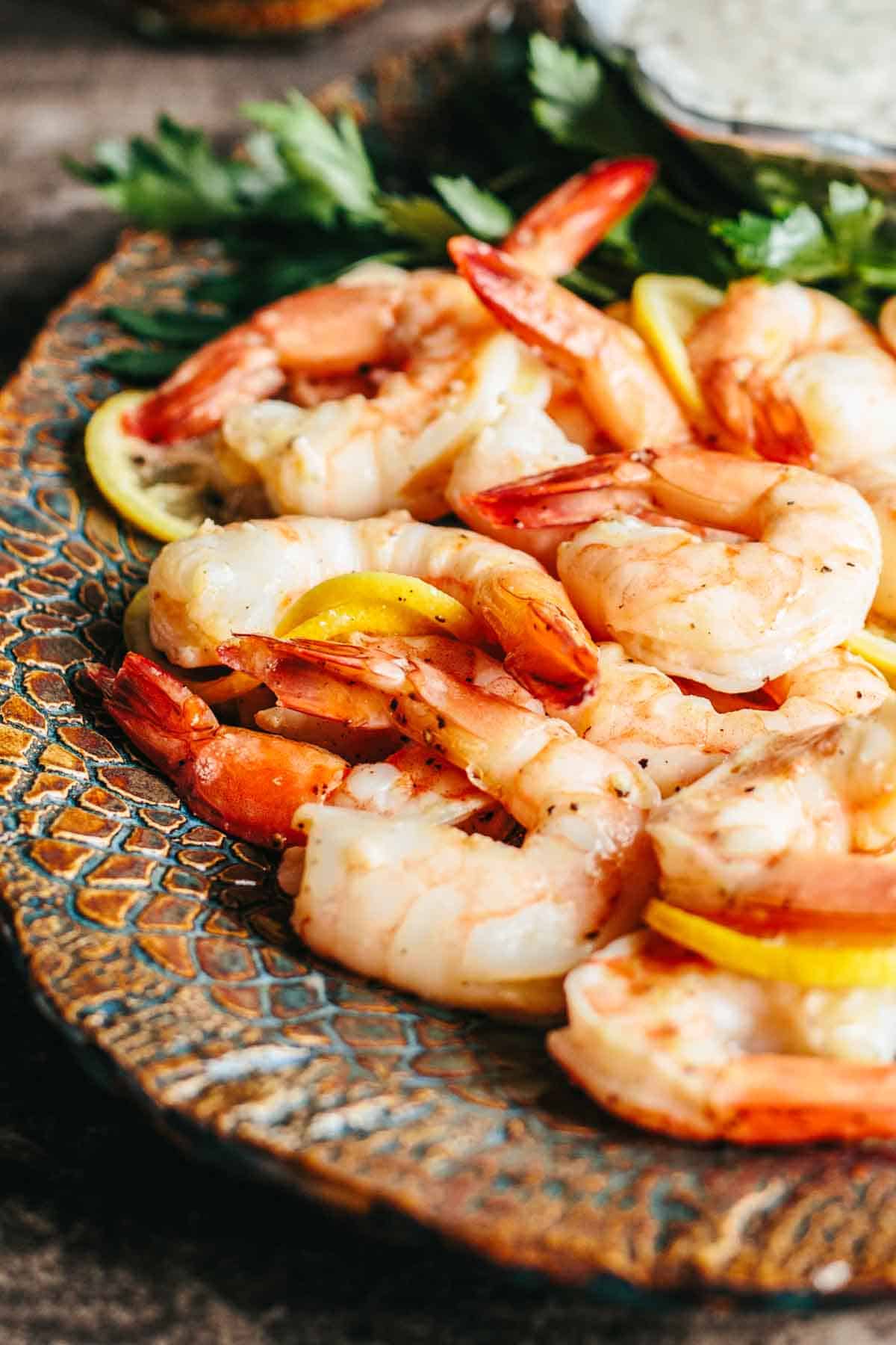 A platter of roasted shrimp with lemon slices.