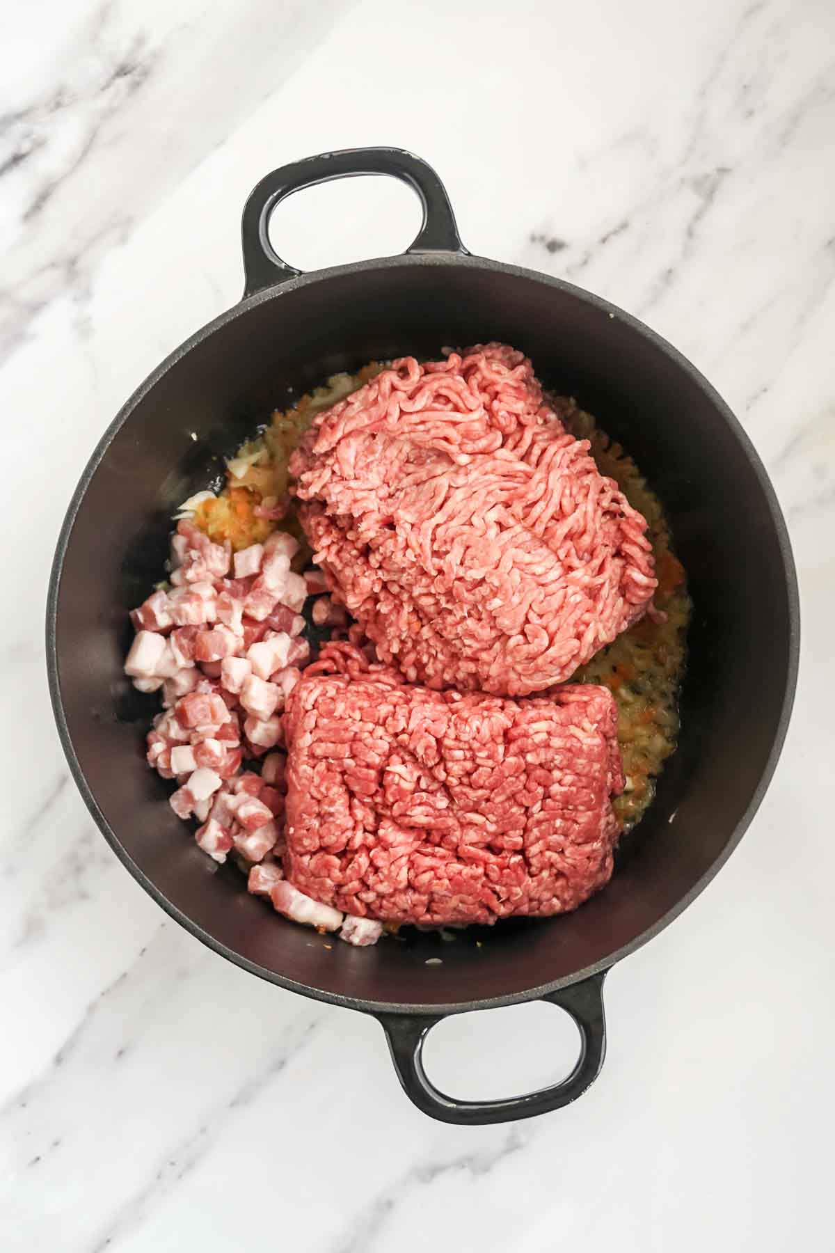 Adding pancetta and ground meat to a pan with vegetables.