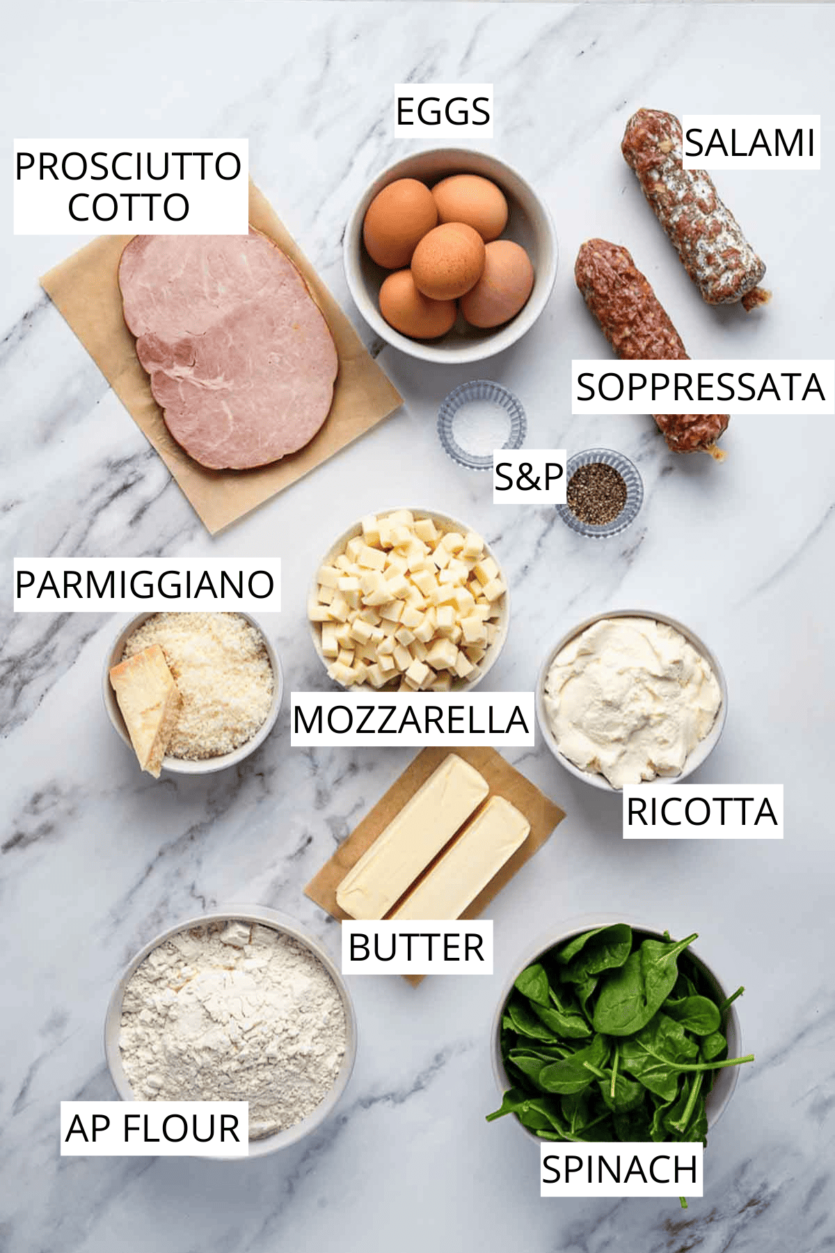 Overhead view of all ingredients for Italian Easter pie laid out on a marble surface, including meats, eggs, cheeses, spinach, flour and butter.