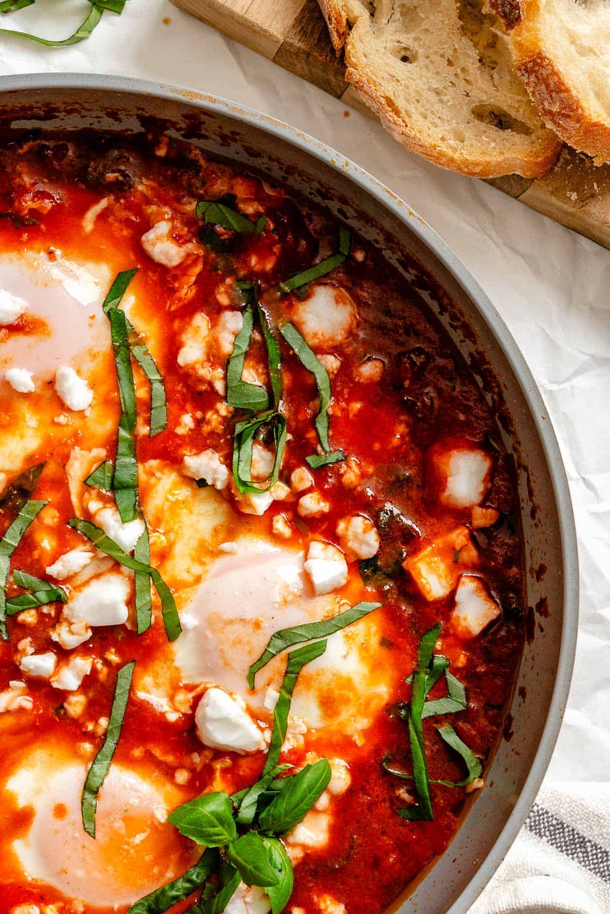 Close-up of eggs in purgatory showing a piece of crusty bread dipped into the runny egg yolk and tomato sauce.