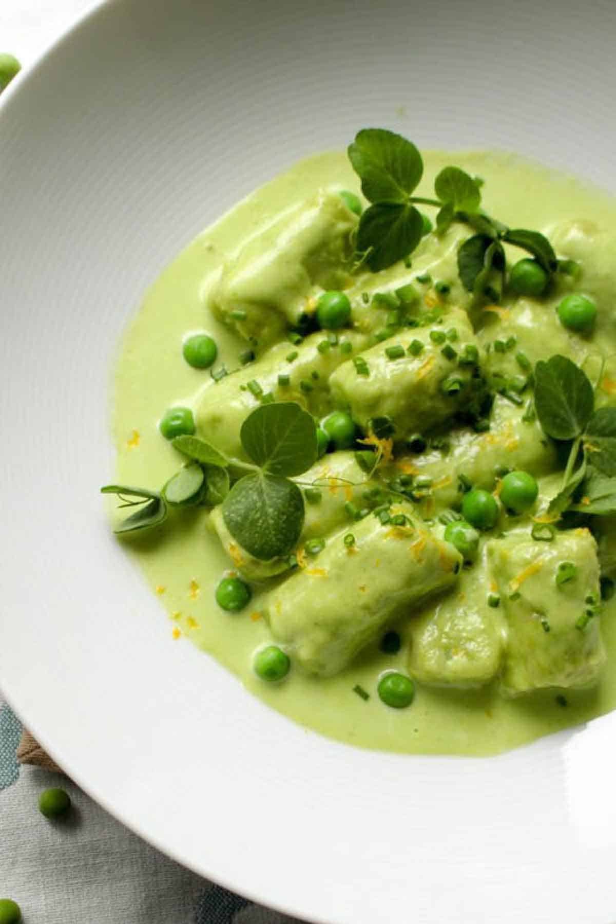 Macro view of tender spring pea gnocchi topped with fresh herbs and bright green peas in a silky sauce.