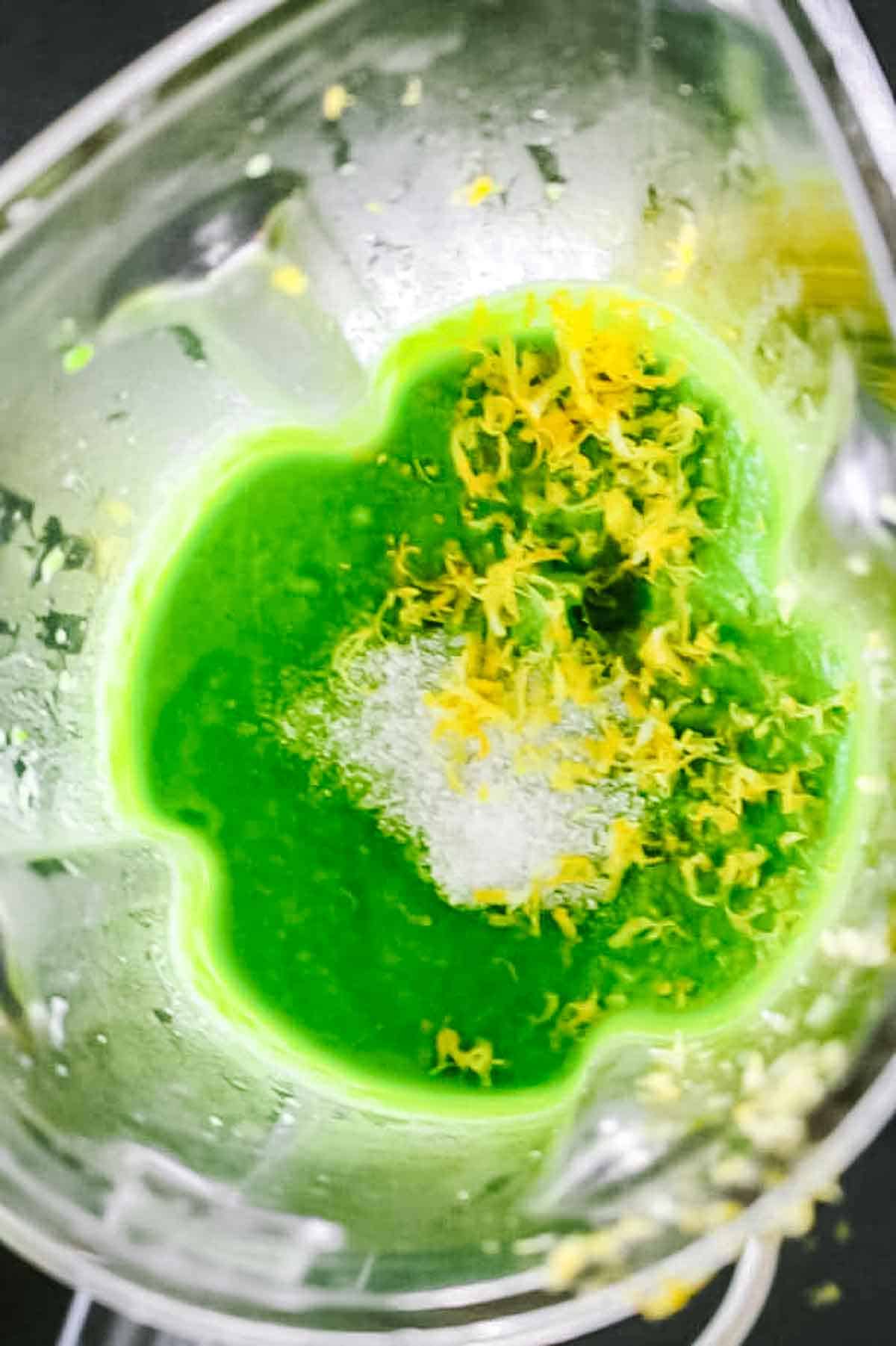 Blender containing bright green pea puree with lemon zest and salt being prepared for gnocchi sauce.